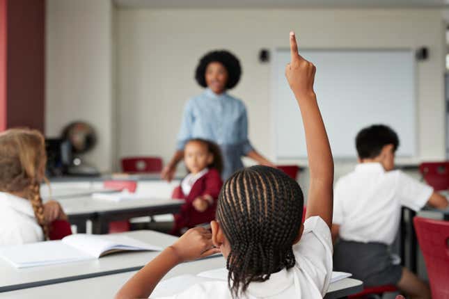 Black child raising hand in classroom 