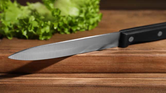 A utility knife on a cutting board with lettuce.