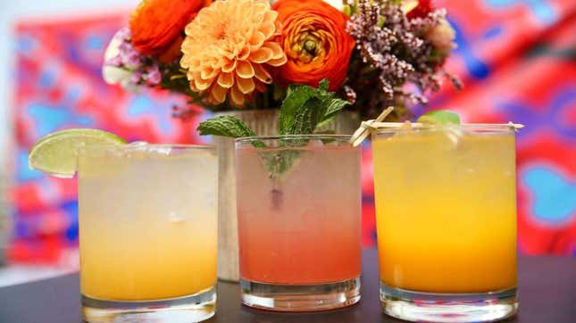 Three colorful cocktails beside vase of flowers
