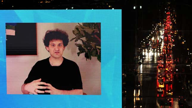 Sam Bankman-Fried on a screen for New York Times Dealbook summit with cars flying by on a New York street.