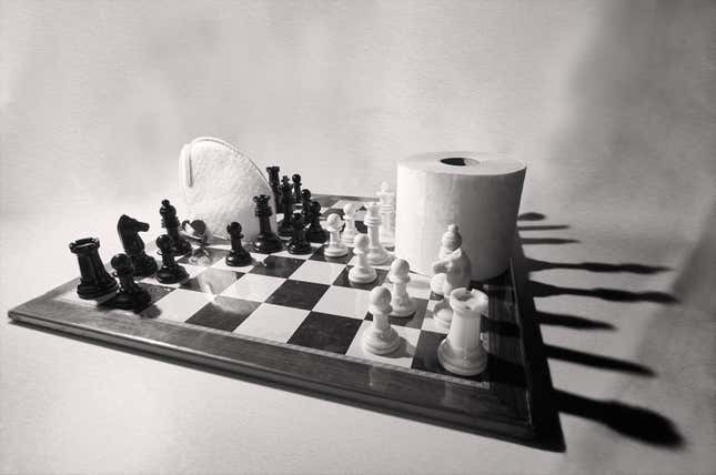 A chess board with a roll of toilet paper and a mask.