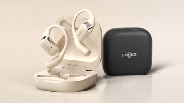 The Shokz OpenFit wireless earbuds shown in beige along with their matching charging case, next to the black version of the charging case.