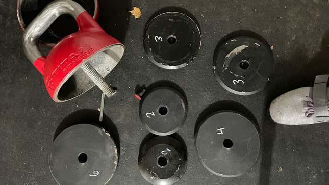 Adjustable kettlebell open (it's red, half of it is in the top left corner) with plates scattered around. They are labeled with their weights.