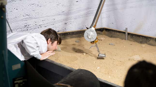 An engineer at NASA’s Jet Propulsion Laboratory observes the COLDArm being tested in a bed of simulated lunar soil.