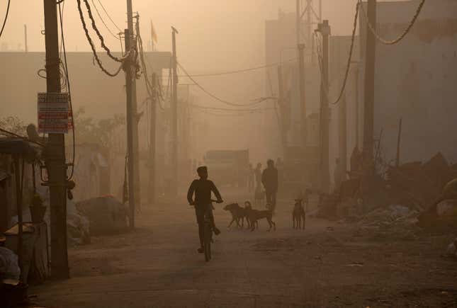 A boy rides his bike in a neighborhood near the Bhalswa landfill, as smoke from the fire fills the air.