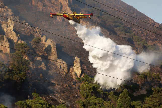 A firefighting plane drains water on a wildfire on the mountain in Altofonte near Palermo, Italy, Wednesday, July 26, 2023.