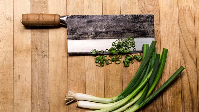 A cleaver with scallions on a cutting board.