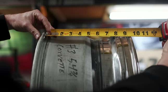 A person measures a custom wheel for a car with a tape measure