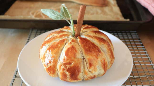 A baked brie shaped like a pumpkin sits on a plate.