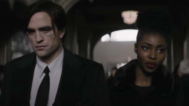 Bruce Wayne and Bella Real, both in black, walk down a church aisle at a funeral.