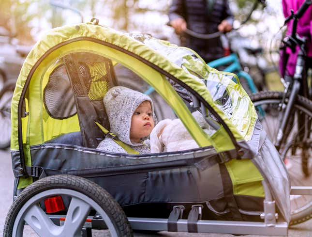 Image for article titled Toddler Riding In Bike Trailer Like Mysterious Aristocrat Arriving For Week-Long Sojourn From London