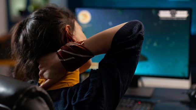 woman sitting at computer at night, rubbing neck in pain