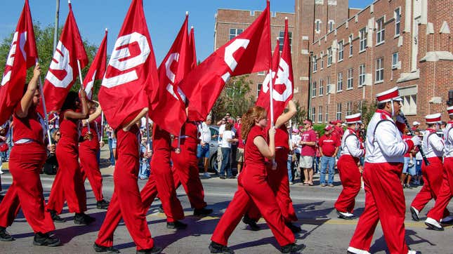 students in marching band uniform carry OU flags in homecoming event