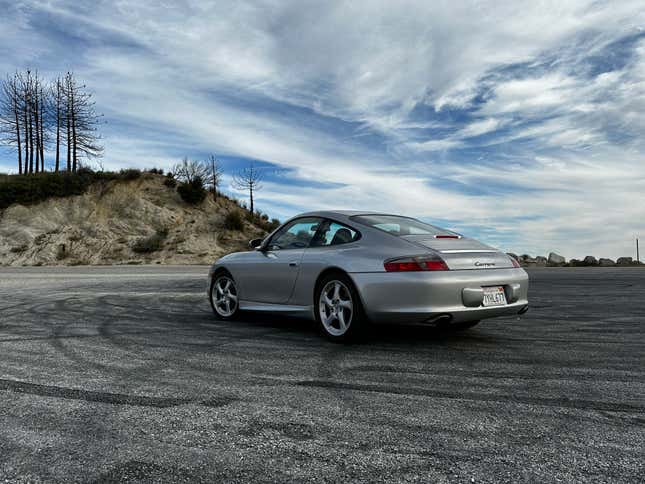 A silver 2003 Porsche 911 is parked under an expansive blue sky, rear three-quarters view.