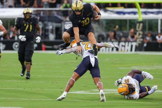 Aug 31, 2023; Orlando, Florida, USA; UCF Knights quarterback John Rhys Plumlee (10) jumps over Kent State Golden Flashes safety Bryce Sheppert (27) during the first quarter at FBC Mortgage Stadium.