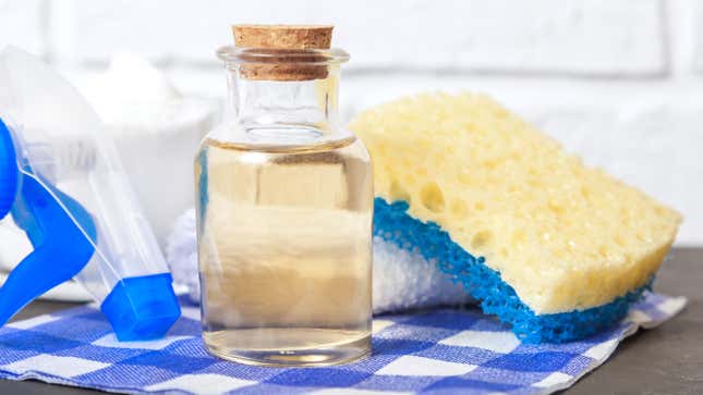 Bottle of vinegar with sponge, spray bottle, and other cleaning supplies