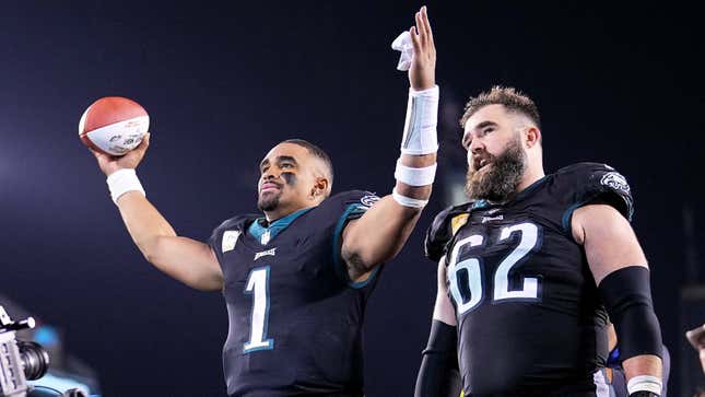 Two NFL players walk together while one holds his arms up in the air. 