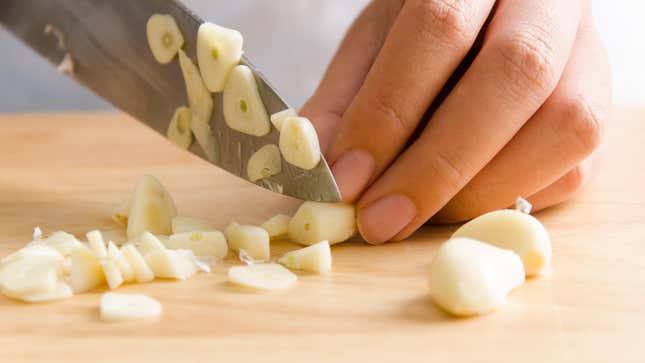 Hand slicing garlic cloves on a cutting board.