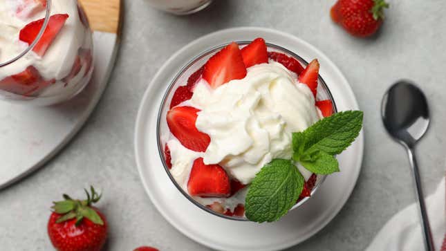 A bowl of strawberries and whipped cream with a sprig of mint.