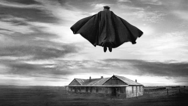 A B&W screenshot from the El Conde trailer of a clocked figure floating in the air over a large, decrepit rural farmhouse