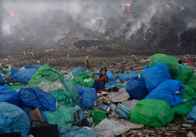A woman looks for usable items in the landfill as the fire rages around her.