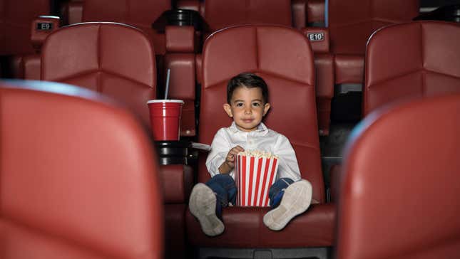 Little boy sitting alone in a movie theater with popcorn and a large soda
