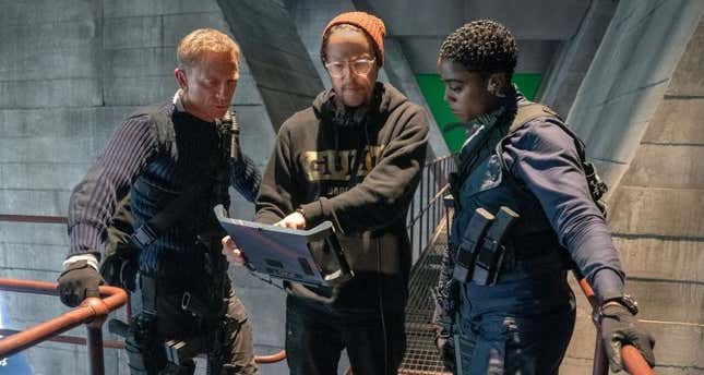Daniel Craig, director Cary Joji Fukunaga, and Lashana Lynch staring at a screen while filming No Time to Die. 