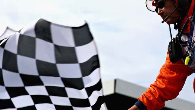 A photo of a marshal waving a black and white checkered flag at an F1 race. 