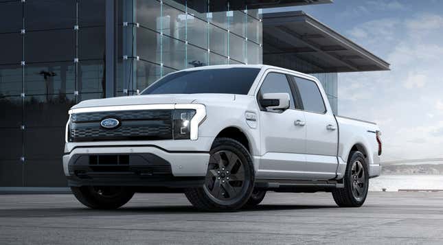 A white 2023 Ford F-150 Lightning is parked in front of a glass building.