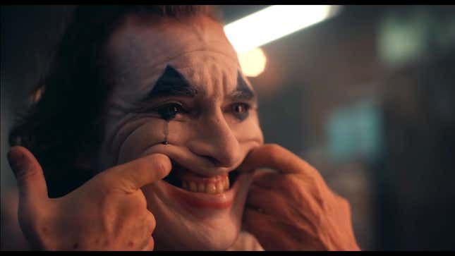 A screenshot of director Todd Phillips' The Joker depicting Joaquin Phoenix (as The Joker) stretching his mouth to force a smile.