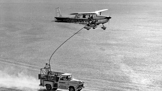 A Cessna airplane refuels in mid-air from a pickup truck in the desert.