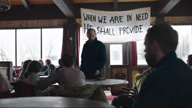David stands before members of his congregation, a sign behind him reading When we are in need He shall provide" behind him.