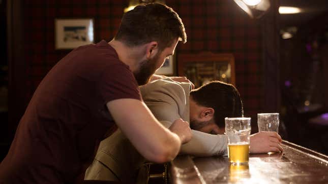 concerned man checking on friend who is asleep on a bar with an empty beer glass