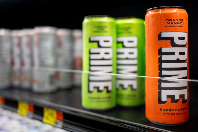 Green and orange cans of Prime Energy on a refrigerated supermarket shelf.