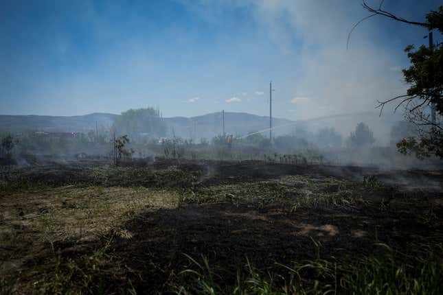 A firefighter directs water on a grass fire on an acreage behind a residential property in Kamloops, British Columbia, on June 5, 2023. 