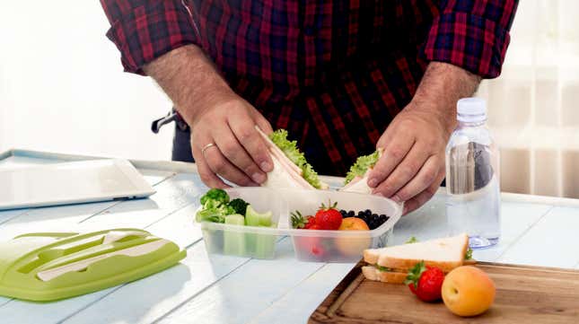 Man packing sandwich and fruit into reusable lunchbox 