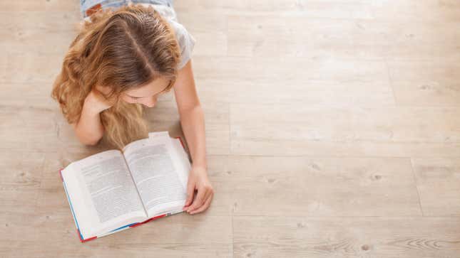 A young girl lying on the floor reading a book