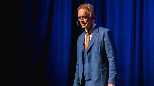 Jordan Peterson on stage with a microphone in his ear, wearing a blue suit.