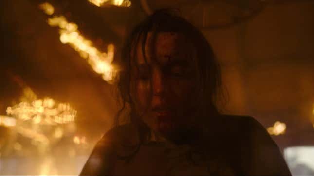 Ellie looks bloody and shaken as a building burns behind her in HBO's The Last of Us.