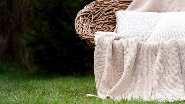 Wicker seat with blanket at pillows outside on grass