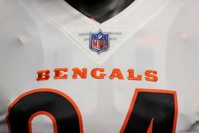 A closeup of a white football jersey with "Bengals" written in orange above black numbers outlined in orange is shown.