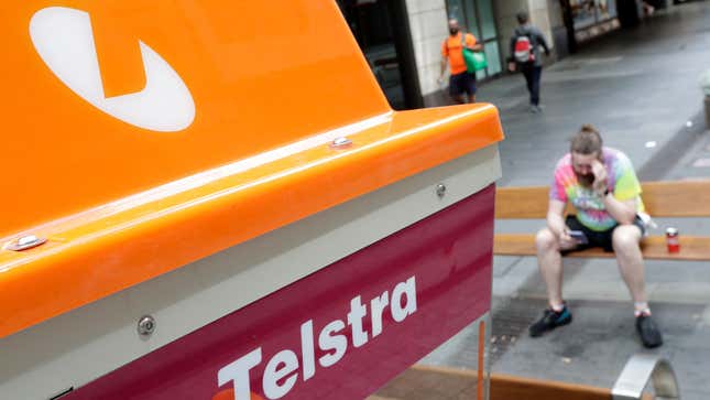A man uses a mobile device while sitting near a Telstra public telephone in Sydney on Oct. 25, 2021.