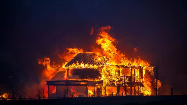 A home burns after a fast moving wildfire swept through the area in the Centennial Heights neighborhood of Louisville, Colorado, against a darkening sky.