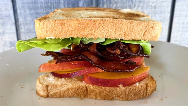 A sandwich on white bread with butter lettuce, bacon, and peach slices