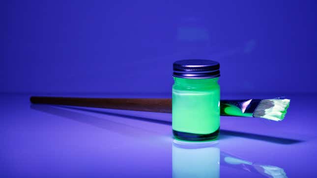 A bottle of glowing green paint under a blacklight 