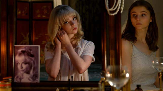 A Anya Taylor-Joy looks in a mirror as Thomasin McKenzie looks on.