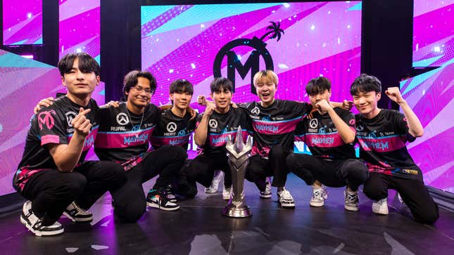 The Florida Mayhem team crouches down in front of the Overwatch League trophy after winning the 2023 Grand Finals. 