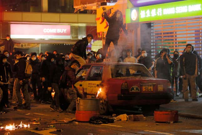 Rioters throw bricks at police in Mong Kok during the Lunar New Year riots. The car is an abandoned taxi cab.