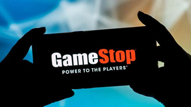 Two hands hold a smartphone that displays GameStop's logo and capitalist motto. 