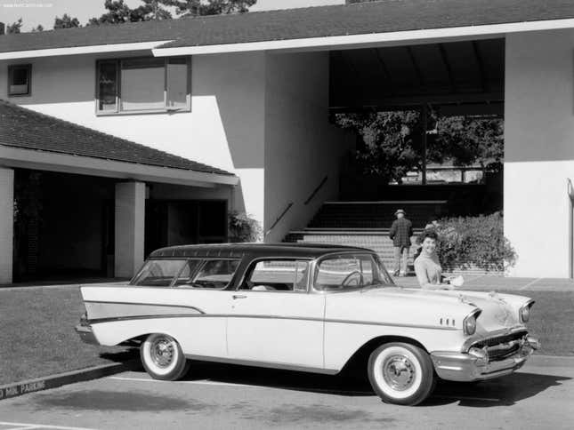 A black and white photo of a 1957 Chevy Nomad in front of an apartment building
